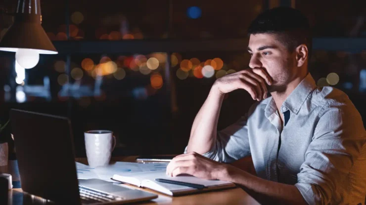 a man sits at night studying information on his computer, reviewing a comparison chart showing details of free nights and weekends electricity plans.