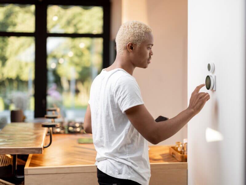 man adjusting a smart thermostat and connecting it to his phone.