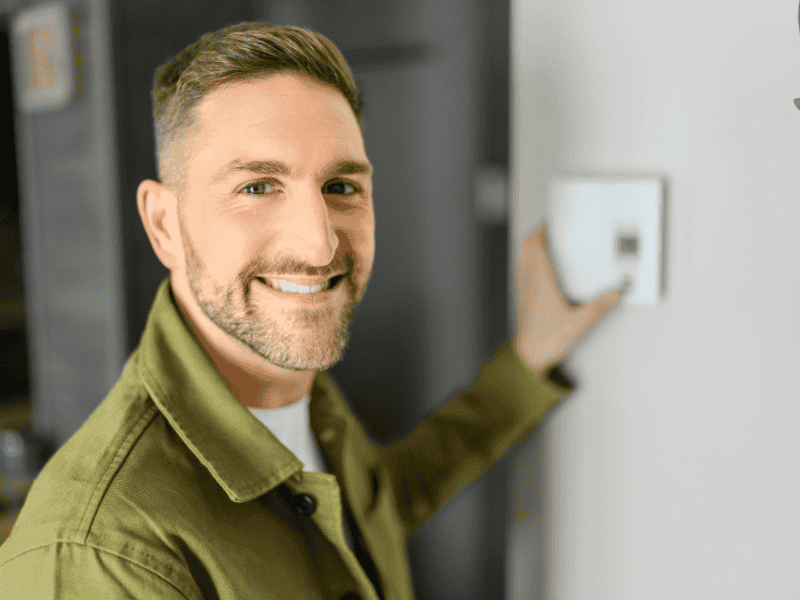 bearded man wearing long sleeved green shirt adjusts his thermostat settings for winter energy savings.