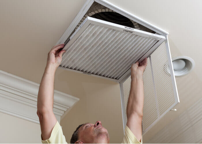 man in yellow shirt changing air filter in central air conditioning system for home office