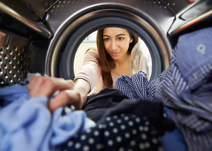 save on electricity with these laundry room tips. image shows woman taking clothes out of the dryer. 
