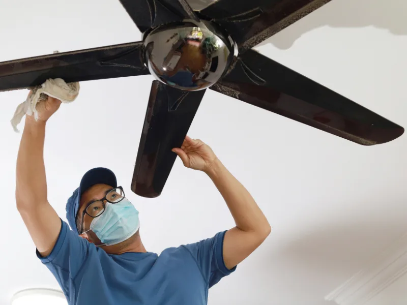 man cleaning dust from ceiling fan and flipping the switch to run counterclockwise in spring and summer.